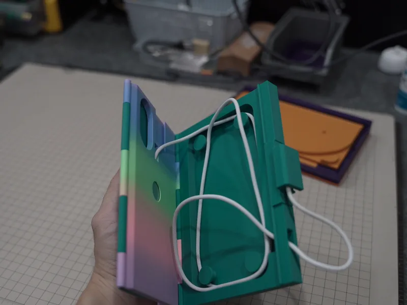 The green prototype open, a white cable hooked into clips on the base, wound untidily