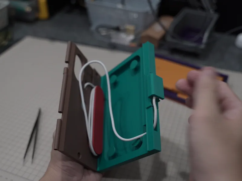 A brown prototype with a red winding spindle, a hand winding the cable