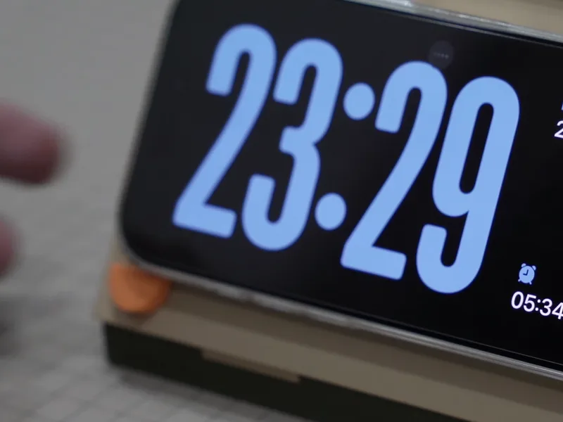 An iPhone lying sideways on the dock, showing the StandBy clock