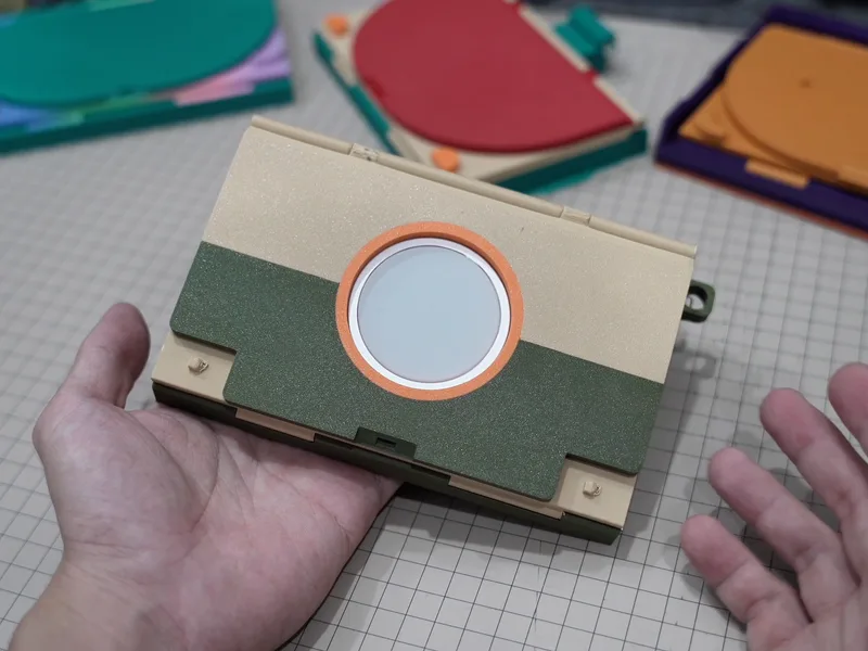 The fourth prototype in sand and olive, closed, an orange ring around the charging puck