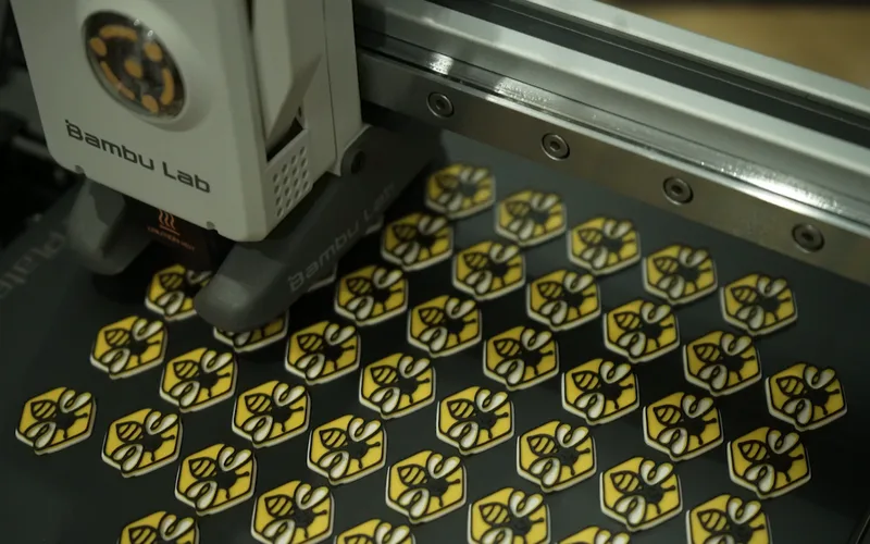 Máy in 3D đang in một bàn đầy logo con ong màu vàng đen