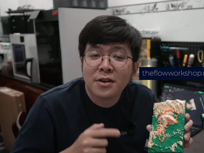Tay cầm sa bàn địa hình in 3D với đường chạy đỏ, bảng theflowworkshop.com phía sau
