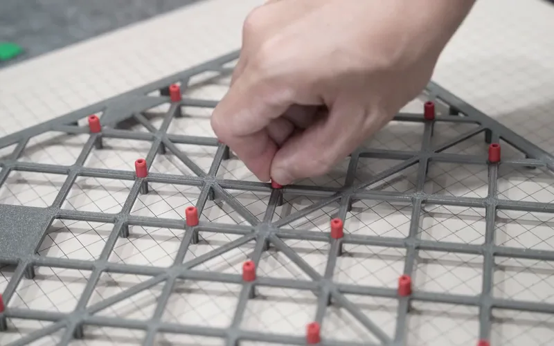 A hand pushing a red pin into the grey tile